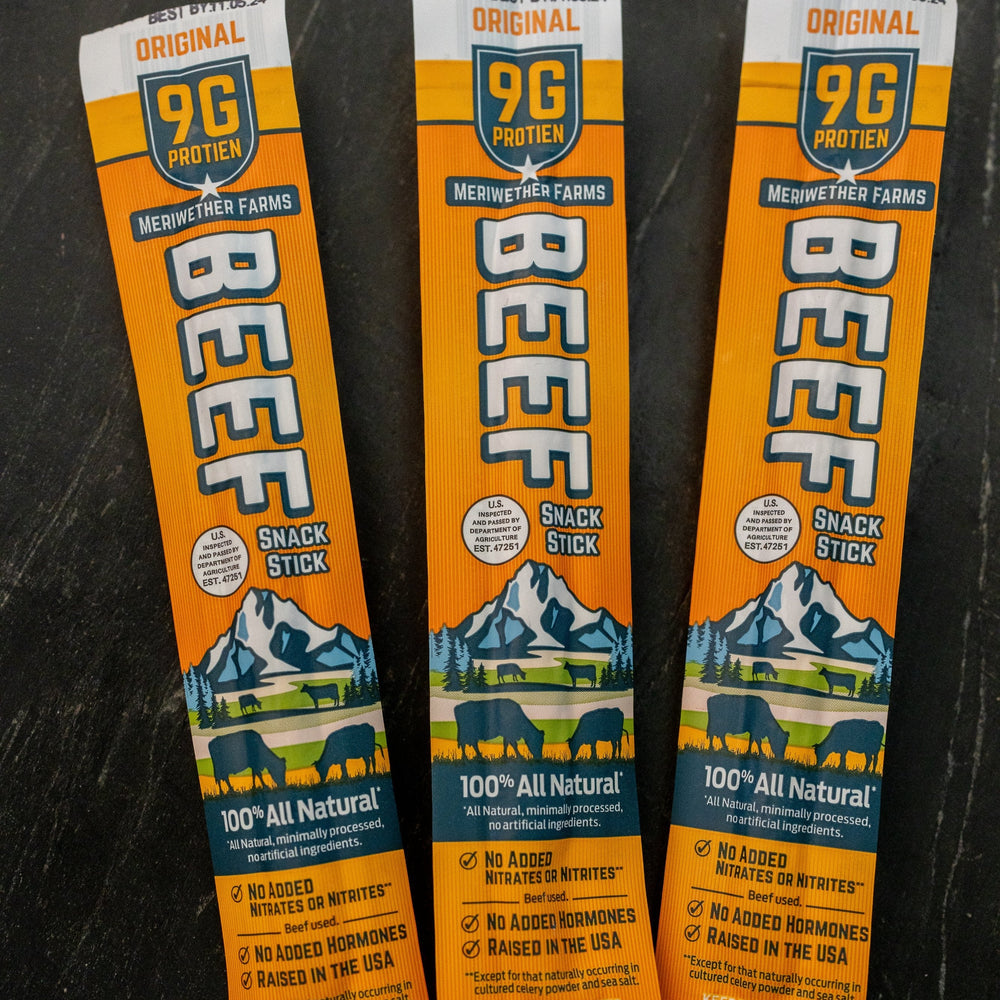 Three packages of Meriwether Farms beef snack sticks on a dark surface